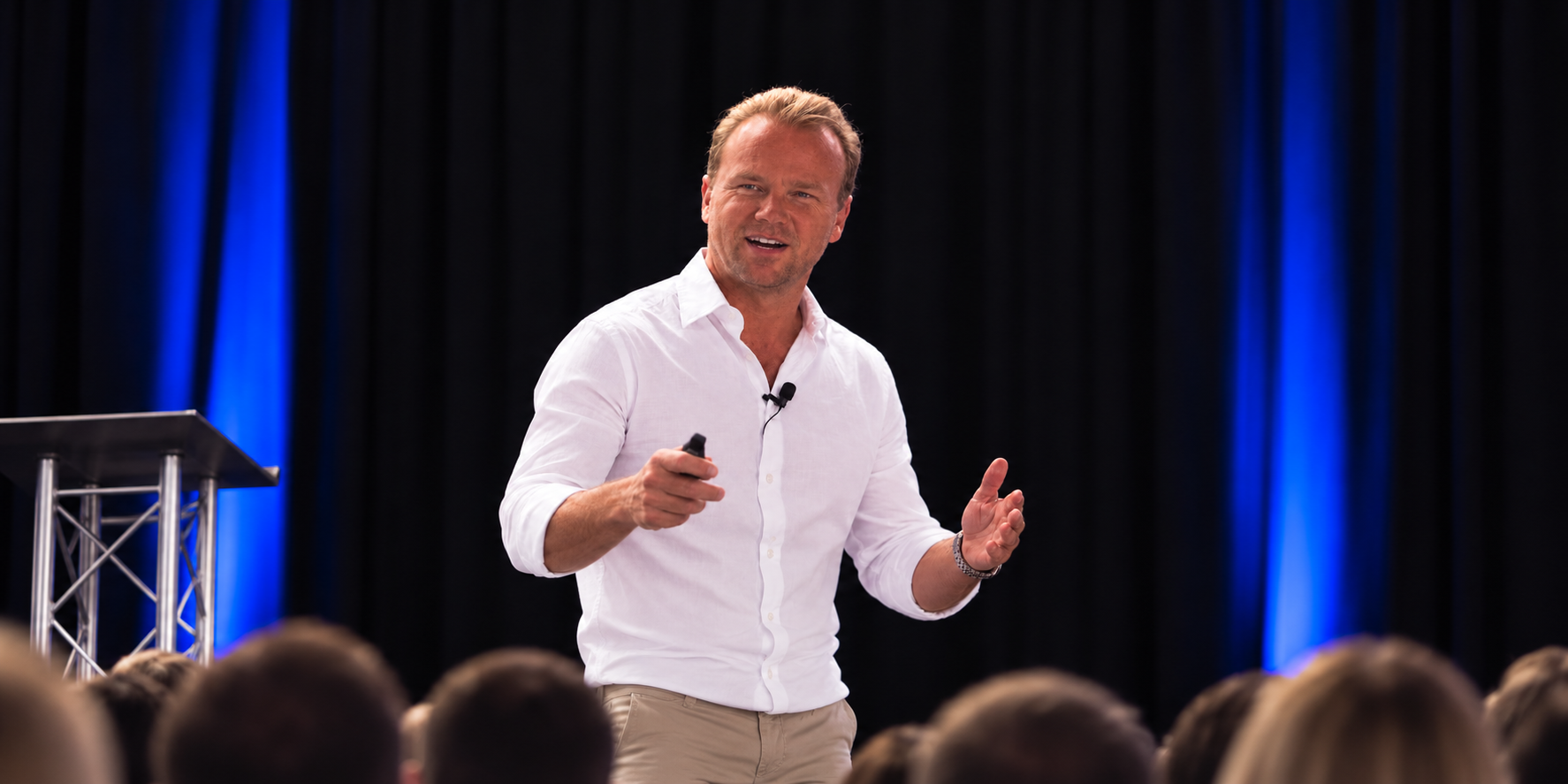 Richie Matthews speaking on stage in a white shirt, gesturing to a conference audience